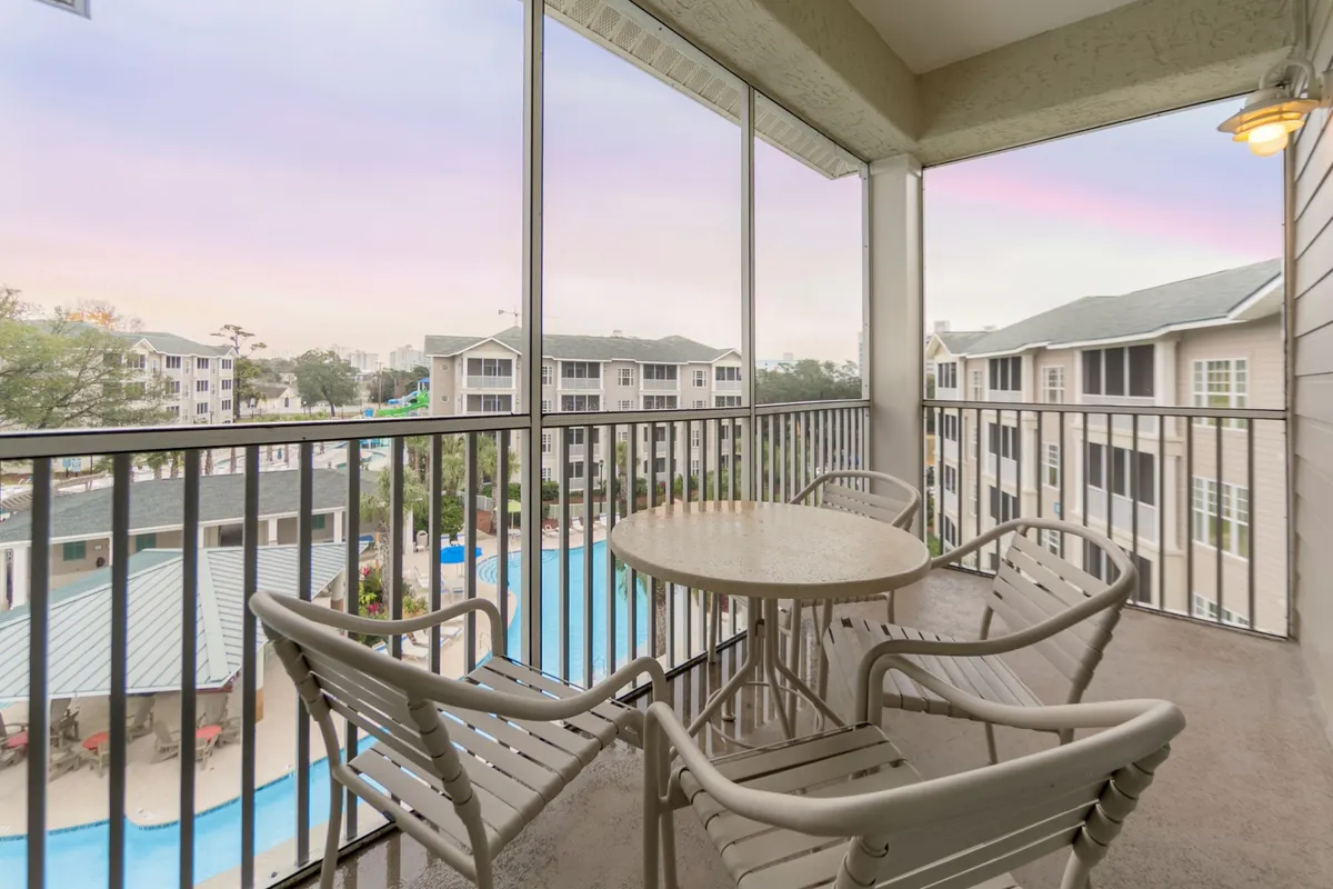 A tranquil view from a private balcony overlooking the resort pool, with comfortable outdoor seating and the surrounding resort buildings. The scene evokes peaceful morning moments or cozy evenings, highlighting opportunities for couples to enjoy serene, shared experiences overlooking the pool and grounds.