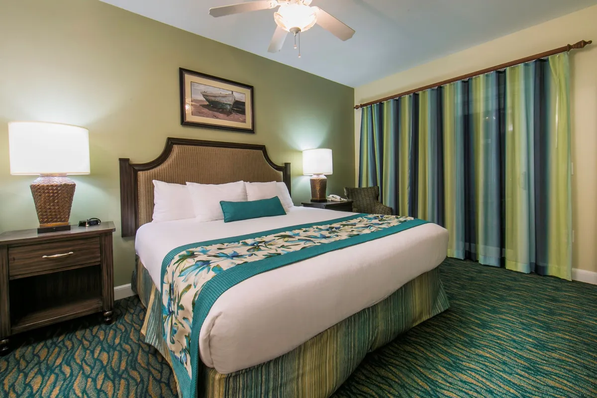 A serene King bedroom featuring a bed with a decorative quilt, matching nightstands with lamps, striped curtains, and tasteful wall art. The room radiates comfort and tranquility, perfect for restful nights and quiet moments.