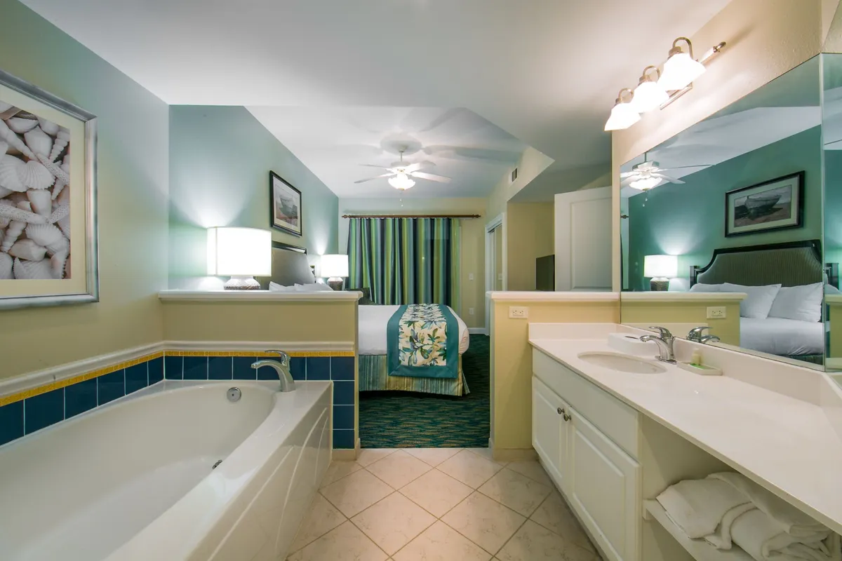 This interior scene captures a serene bathroom with a soaking bathtub, vanity, comfortable bed, elegant window treatments, and decorative artwork. The overall atmosphere is calming and designed to encourage relaxation and pampering after a day of activities.
