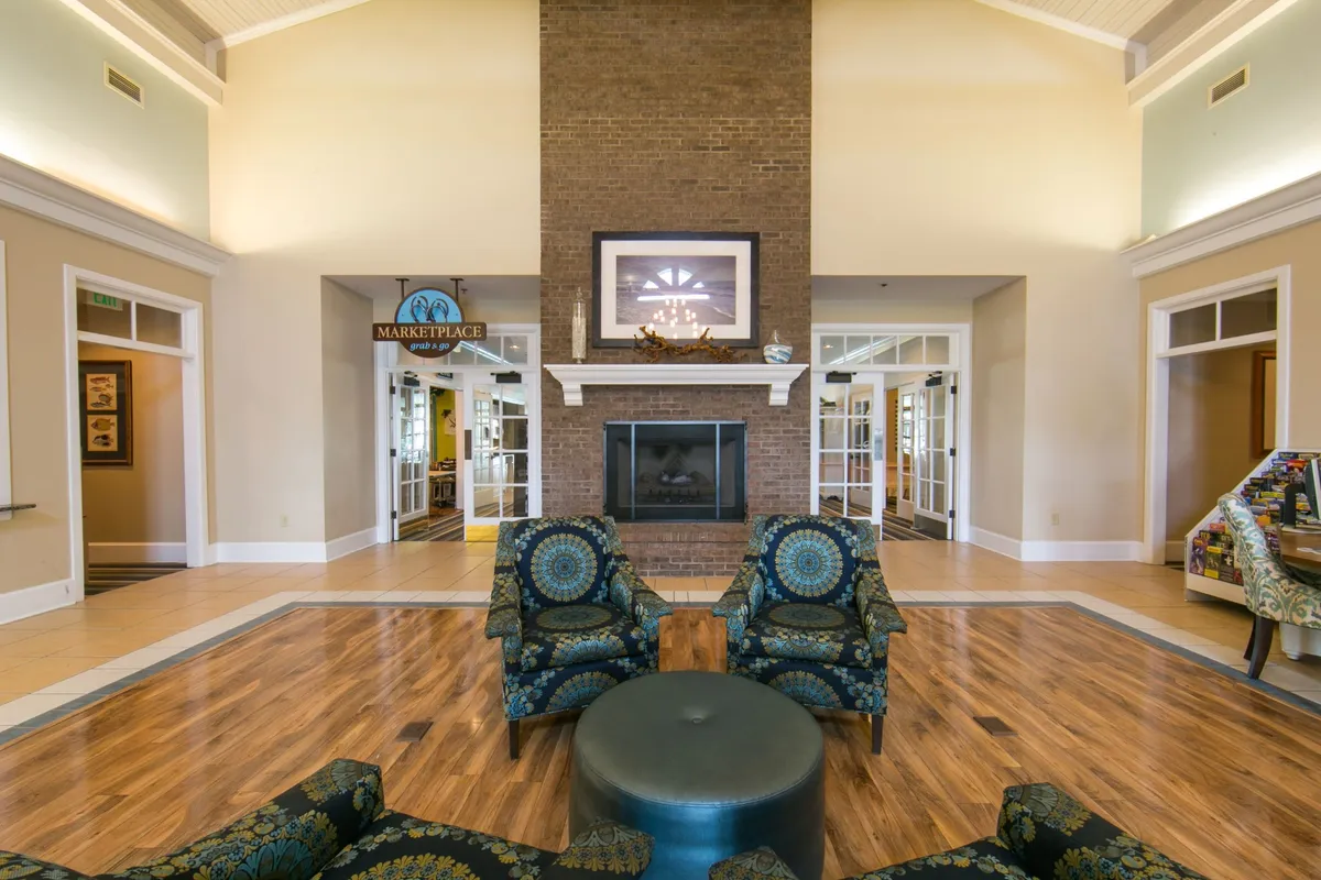 A cozy interior living room featuring a welcoming seating area arranged around a crackling fireplace. The room includes plush armchairs and a sofa, creating an inviting atmosphere perfect for both relaxation and socializing. A marketplace sign subtly hints at resort amenities, and warm lighting enhances the sense of home comfort.