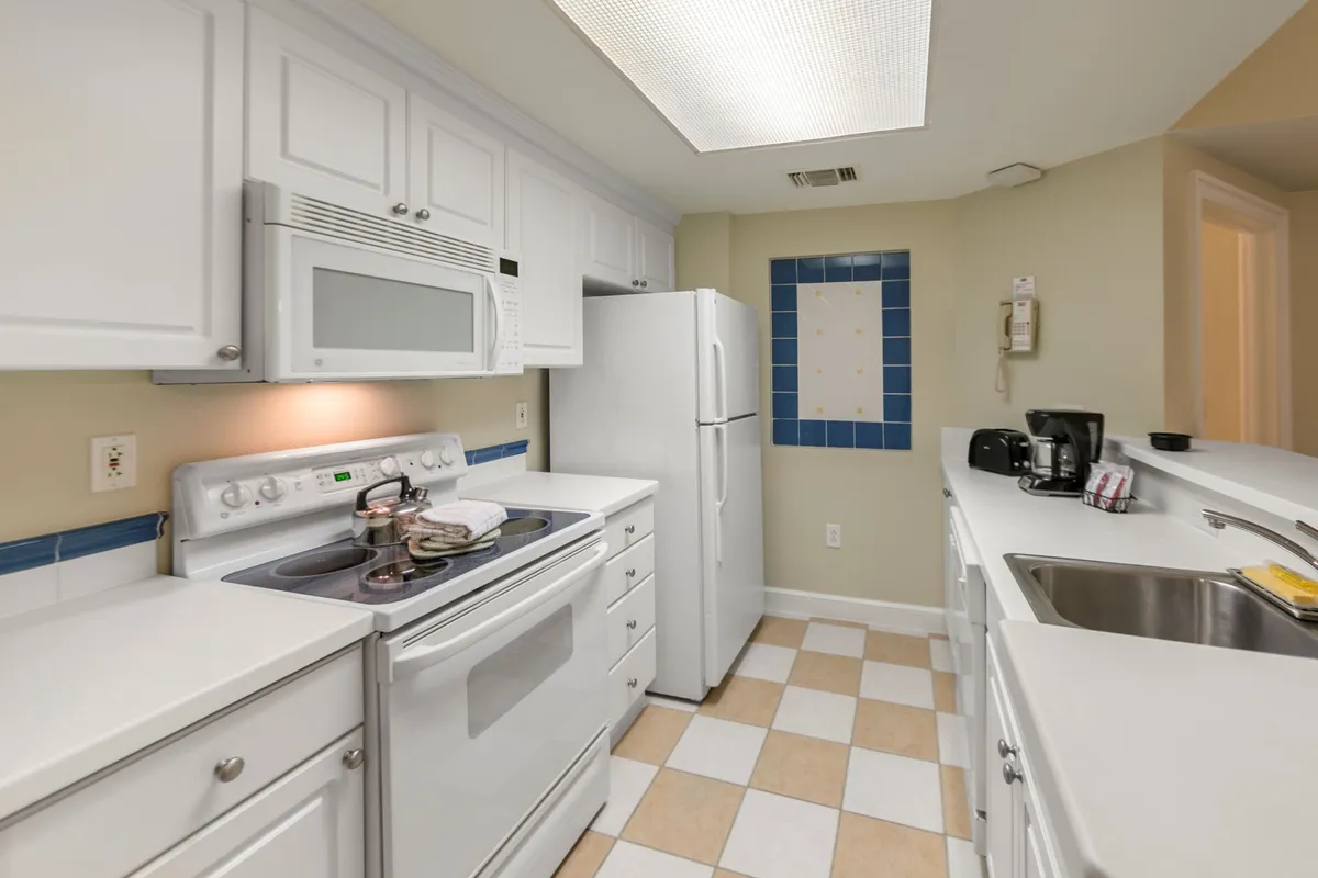 A bright, modern kitchen with white cabinetry, stainless steel appliances, checkerboard flooring, and a striking blue tiled accent wall. The inviting layout makes it ideal for cooking, family meals, and hosting gatherings, while practical touches suggest a space where memorable meals are easily prepared.