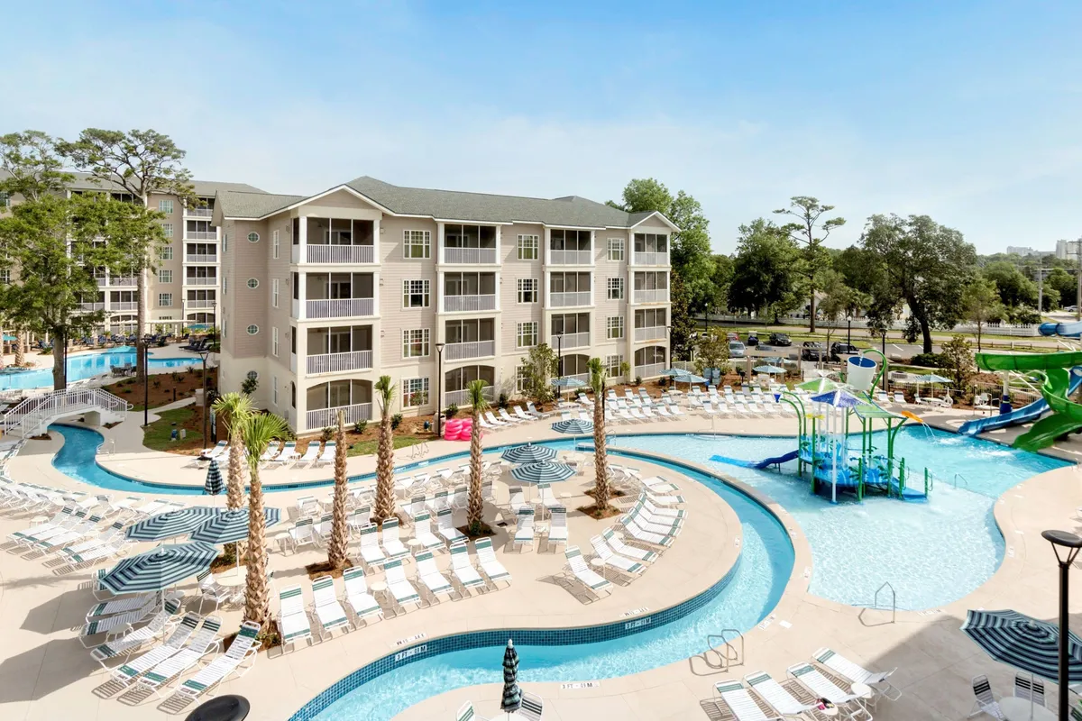 This lively outdoor scene captures multiple swimming pools, twisting water slides, lush palm trees, lounge chairs, and a vibrant building facade. Families are seen swimming, sunbathing, and playing, evoking a sense of joyful summer fun and relaxation.