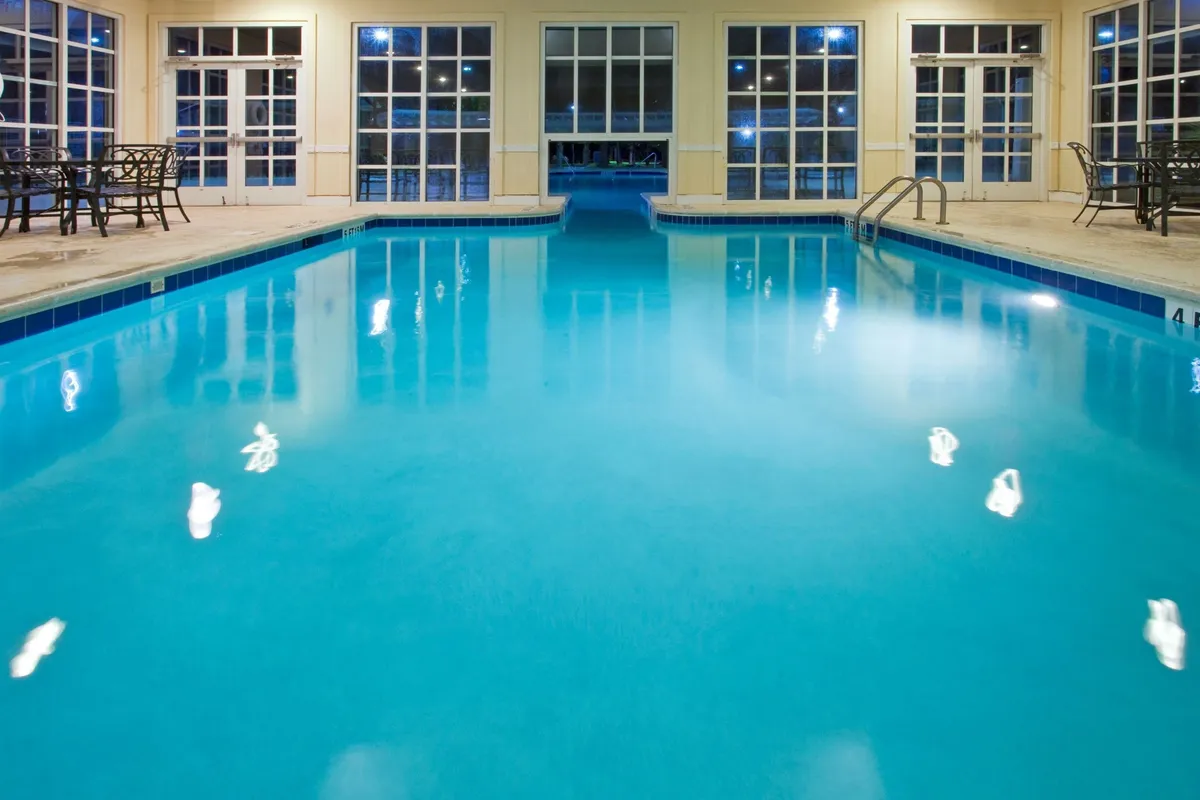 A serene indoor swimming pool bathed in soft lighting, surrounded by comfortable chairs and large windows. The tranquil ambiance conveys year-round enjoyment, regardless of the weather outside.