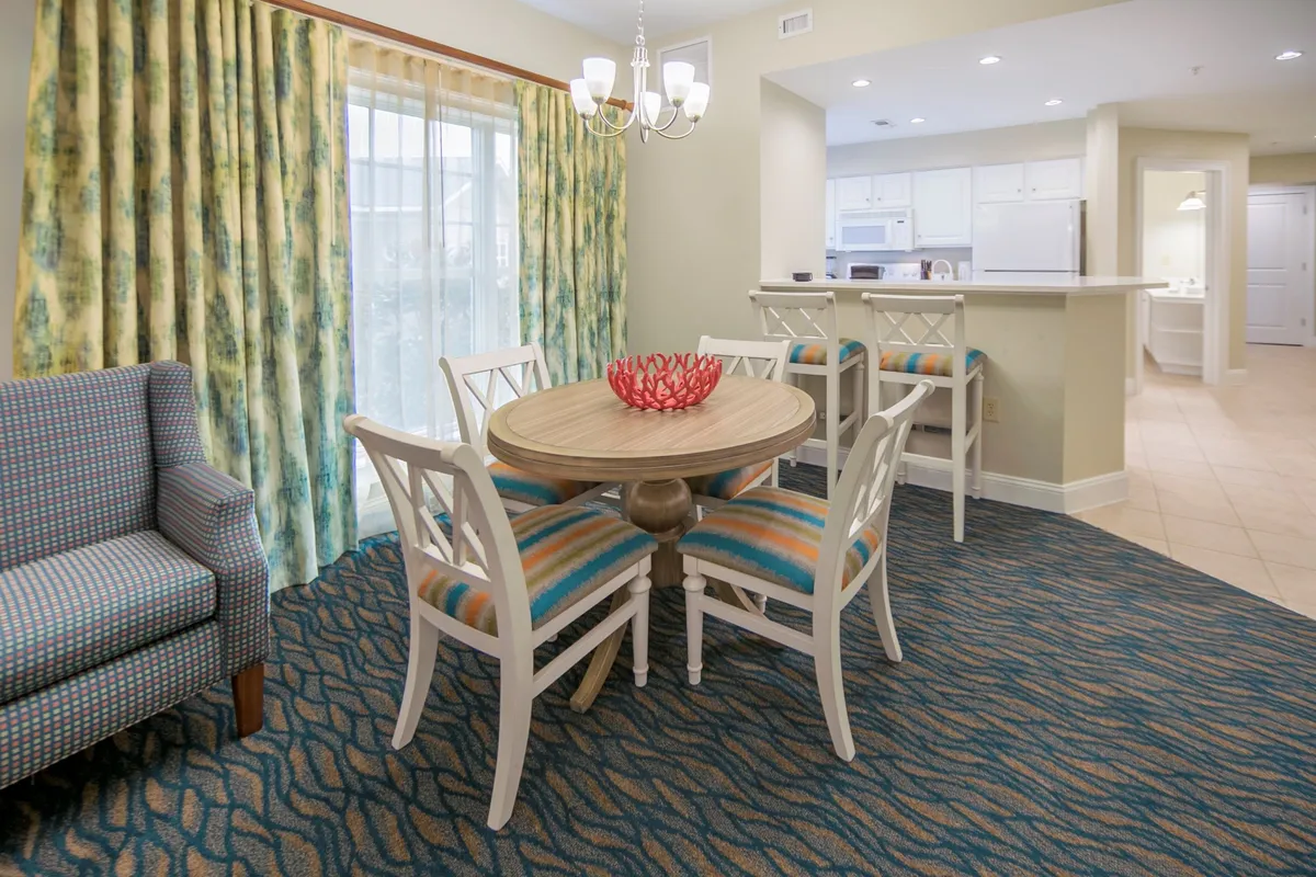 Inside, a vibrant dining area features a large table, striped chairs, and colorful curtains, creating a space for families or small groups to gather and stay organized. The layout feels welcoming and smartly designed for effortless living.
